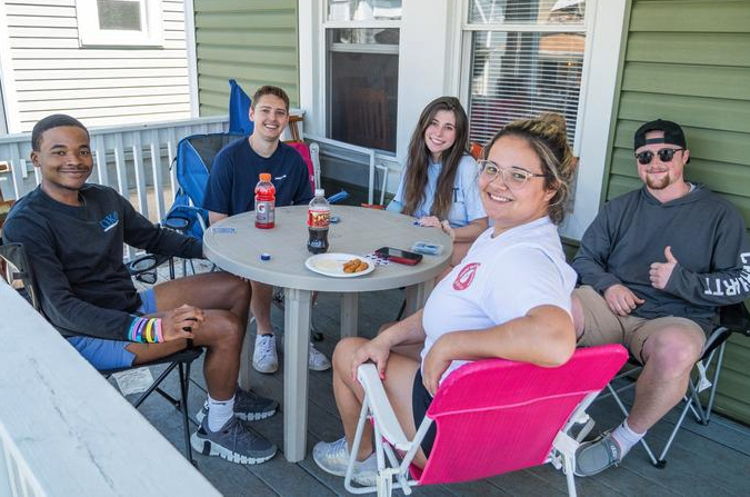 Young adults sitting in a group smiling on a porch.