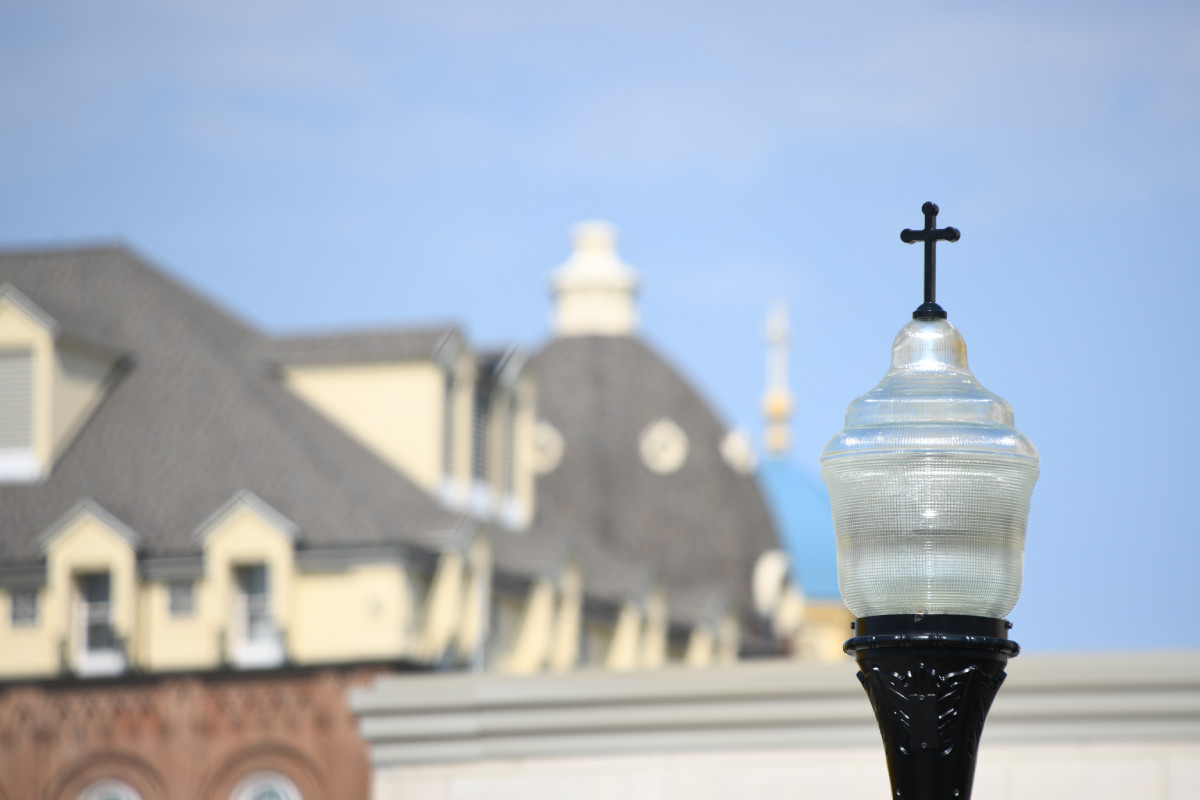 Exterior lamp post with a decorative cross at the top and the University of Dayton campus unfocused in the background