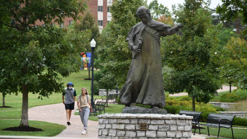 Two students walking by a statue.